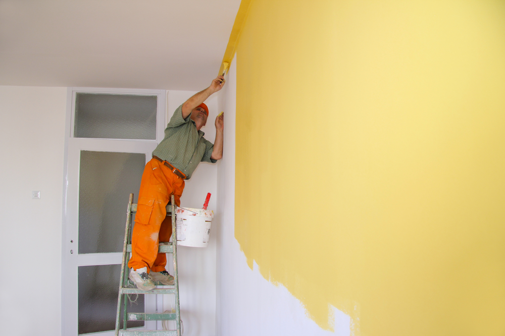 Painter In Action On A Ladder Painting Walls Yellow in Apartment Hiring Apartment Painting Contractors